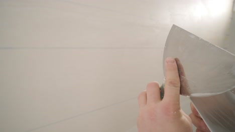 man plastering the walls with finishing putty in room with putty spatula