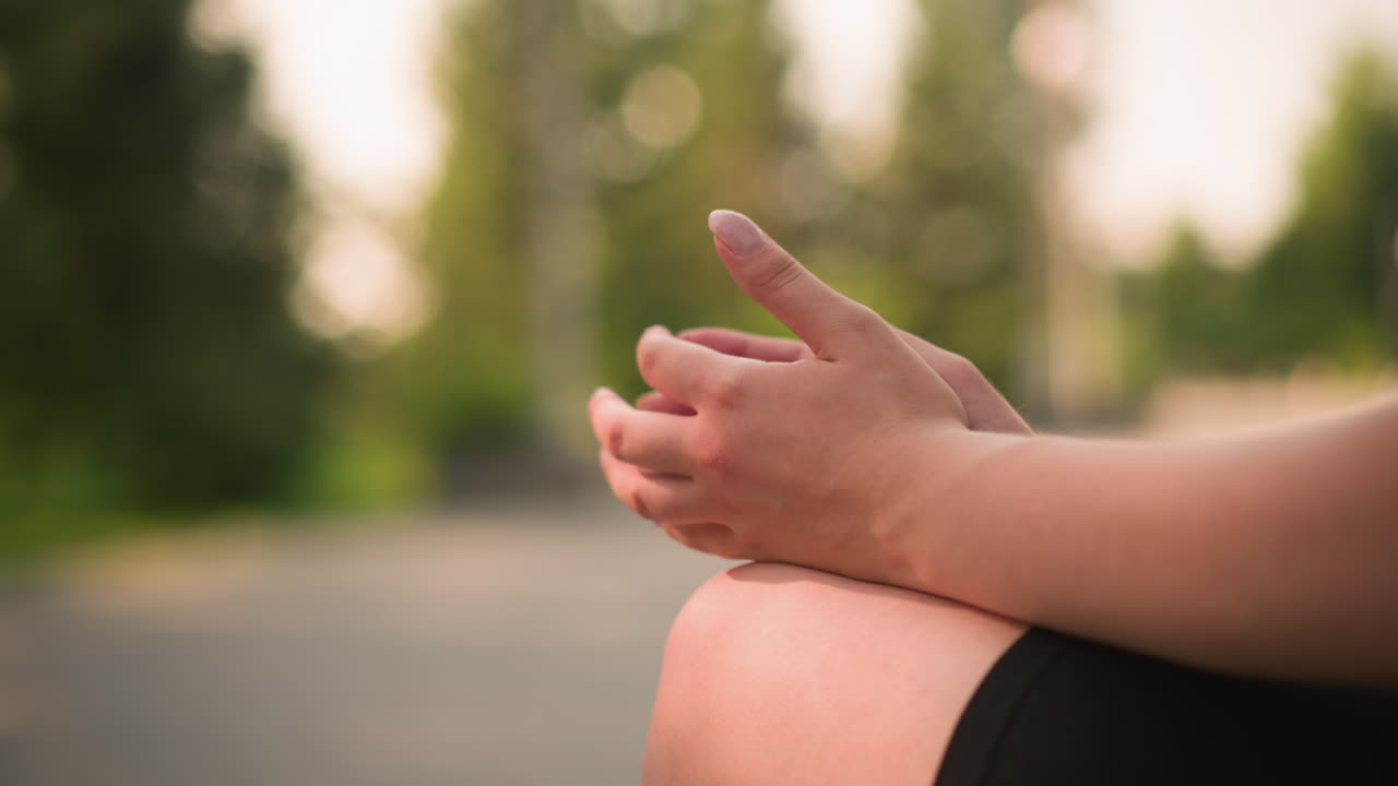 야외에 앉아있는 개인의 부분적 인 시각, 다리를 단하고, 무에 손을 놓고, 따뜻한 빛 아래 다른 손을 부드럽게 고, 녹색을 특징으로하는 부드러운 흐릿한 배경