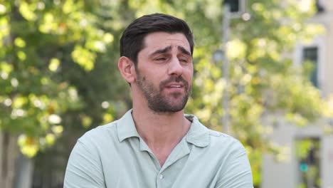 happy man in shrugging shoulders at city park during sunny day