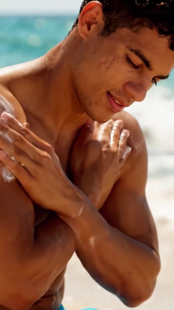 A Young Man Enjoys a Sunny Day at the Beach Applying Sunscreen for Skin Protection Against Harmful UV Rays and Sun Exposure While Having Fun by the Ocean