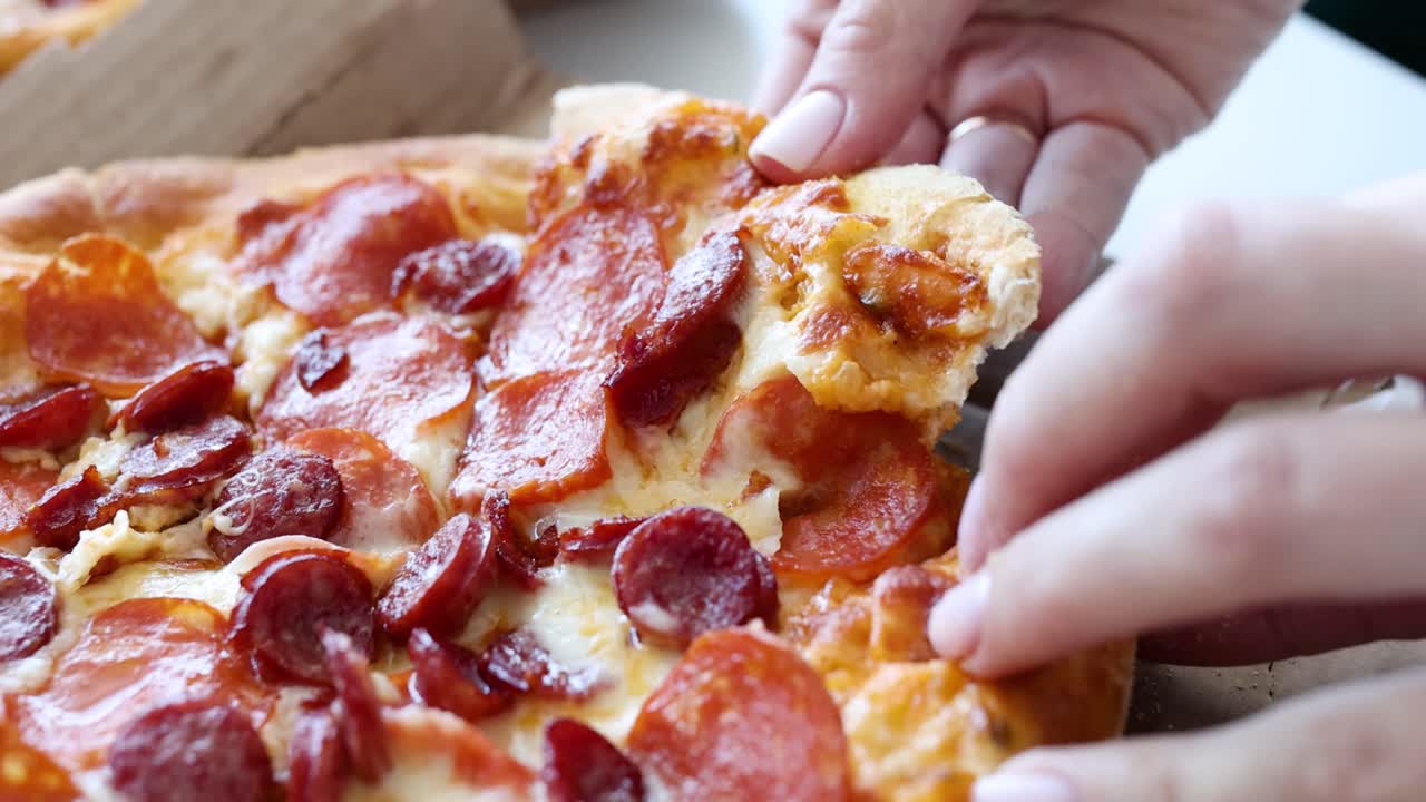 A close-up of a hand taking a slice of pepperoni pizza