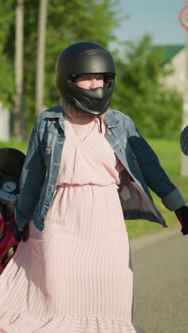 two friends stand near a parked power bike, the woman in pink playfully moves her gown while the other touches her chin in playfully,in a peaceful residential area
