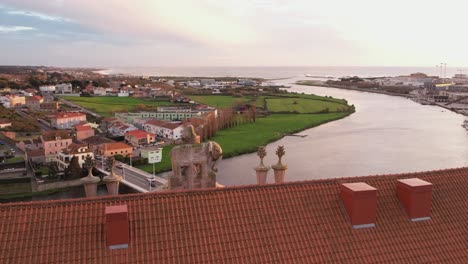 aerial - sunset over river and rooftops in vila do conde portugal with statue