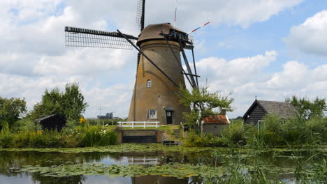 Wunderschöne-Aufnahme-Einer-Windmühle-Mit-Spiegelungen-Im-Wasser-Eines-Flusses-Und-Großen-Schwimmenden-Blättern