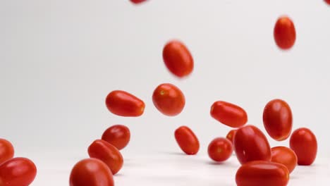 frutas y verduras frescas de tomate de cerezo rojo brillante rebotando en la mesa blanca en cámara lenta