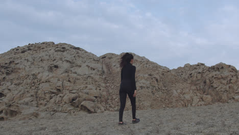 long slow motion shot of a mysterious woman dressed in black walking in the desert between mountains of sand