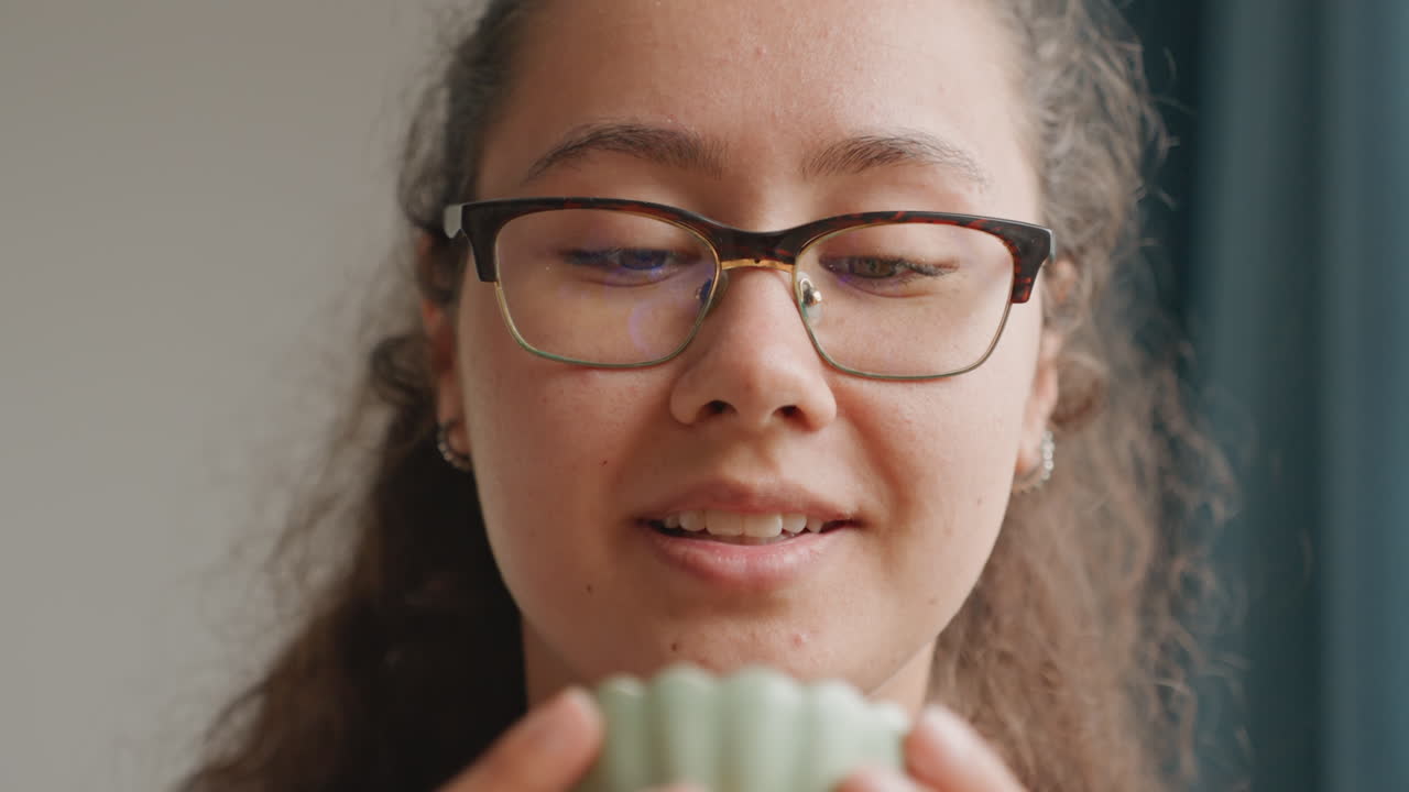 Guest smiling while holding tea cup, leisure traveler expressing gratitude in hotel suite, evening glow through curtains, relaxed portrait with glasses, gentle breathing and contentment