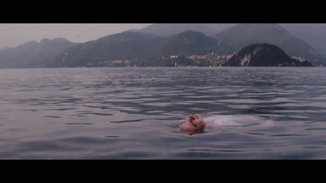 person floating on a lake in front of mountains