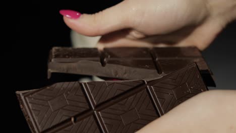 woman breaks black chocolate bar. close-up shot of woman fingers