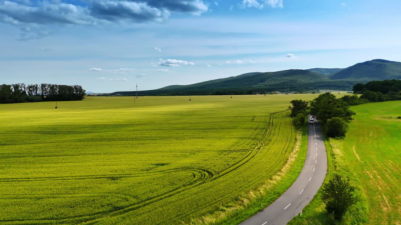 Driving through green countryside. A car travels along a winding road in a lush green landscape under a clear blue sky with distant mountains