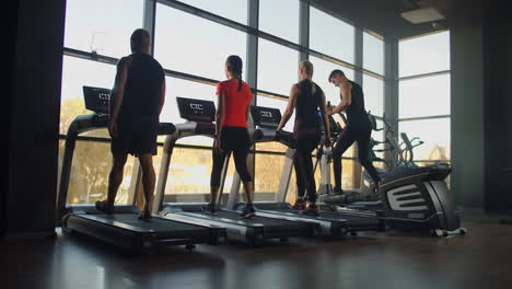 four people young men and women walking on treadmills in the fitness room. start training warm up people before fitness training.