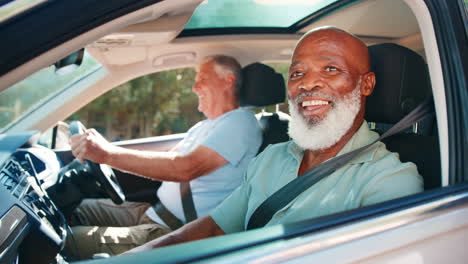 two senior male friends enjoying day trip out driving and sightseeing in car together