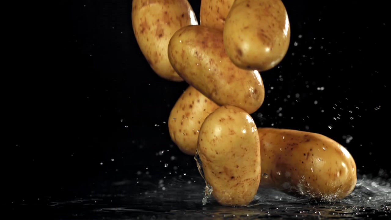Patate fresche che cadono al rallentatore con schizzi d'acqua