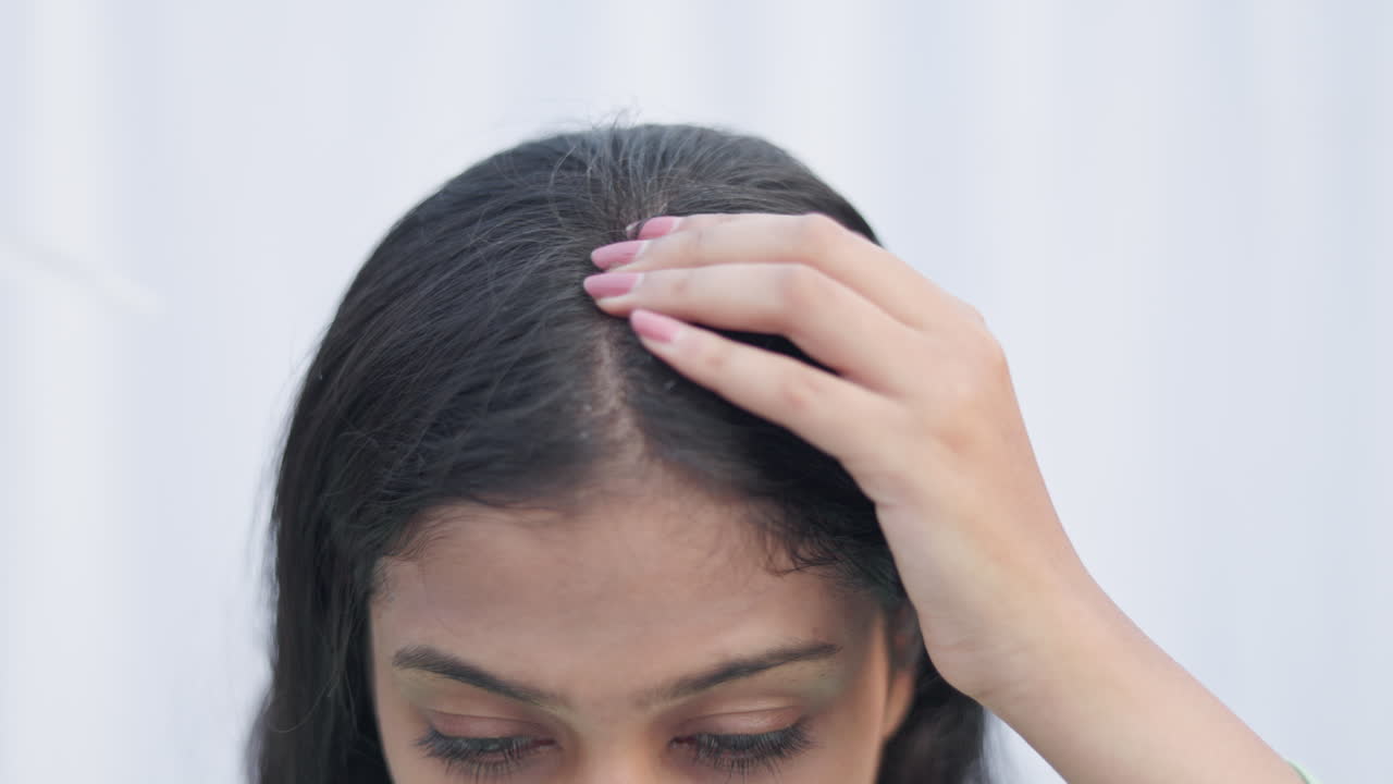 Indian young lady applying essential oil with a dropper on her scalp to treat androgenic alopecia hair loss disease in white background