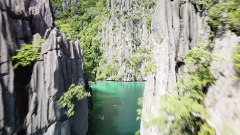 People swimming on in the clear turquoise water in the Philippines on a bright sunny summer day while the camera is going between a narrow cliff. Drone dolly shot