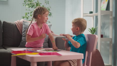 Toddler-boy-glues-dot-sticker-on-sister-cheek-at-table