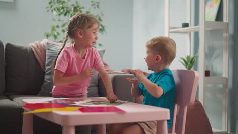 toddler boy glues dot sticker on sister cheek at table