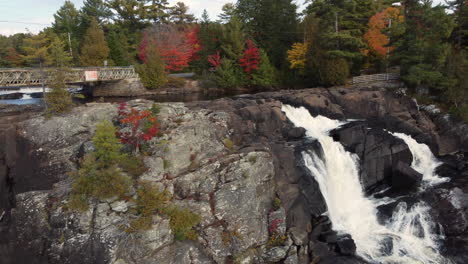 panning shot of waterfalls over rocks on the edge of a forest covered in fall colors