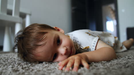 beautiful caucasian child lies on the soft carpet close to camera. baby boy lies moving his little feet, then jumps up and runs away. low angle view.