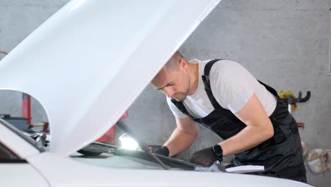 a male mechanic inspecting a car engine in a garage