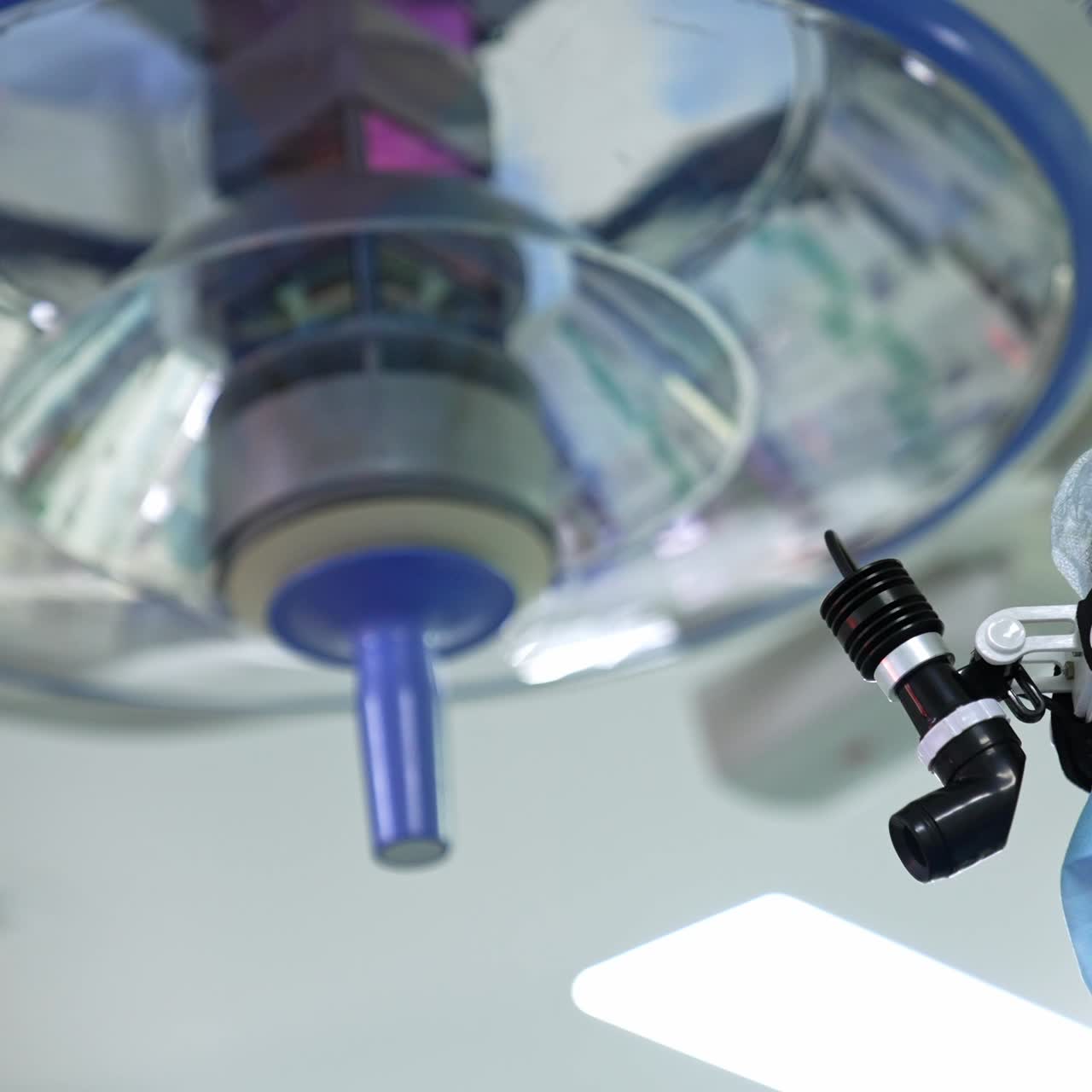 Face of a male surgeon in mask and led headlight. Big round surgical light equipment at backdrop in blur. Low angle view