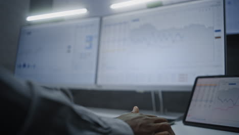 stock exchange trader in wireless headphones having call, monitoring real-time stocks, exchange market charts on multi-monitor desk setup. african american investment agent working. vertical shot.