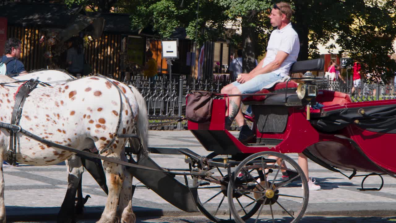 Un cocchiere seduto su una carrozza rossa mentre turisti e pedoni passano in una piazza soleggiata.