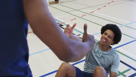 diverse male basketball players helping each other up during game at indoor court, slow motion