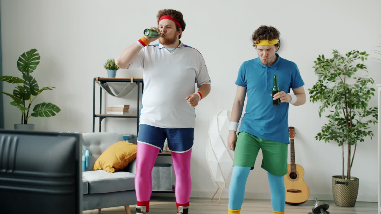 Two Men in 80s Workout Attire Dancing While Drinking Beer