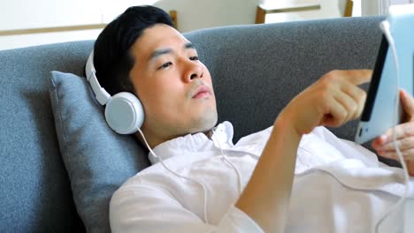 man listening to music on digital tablet while lying on sofa 4k