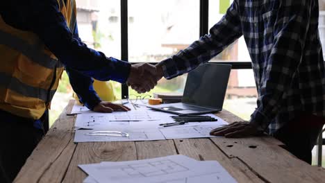 two civil engineer or architect holding helmet and handshaking after mega project done. handshake engineer sketching a construction project concept.4k side view.