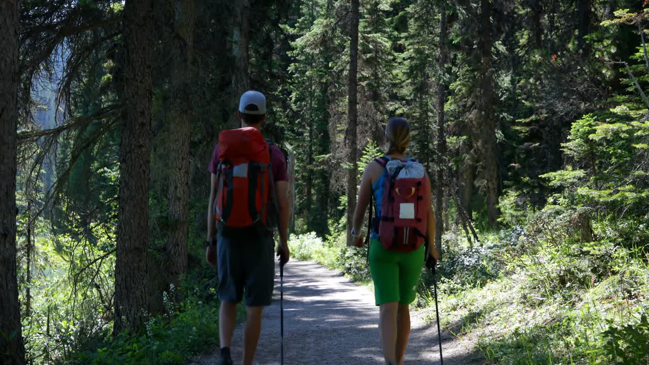 Front view of young caucasian hiker couple with backpack hiking in dense forest 4k