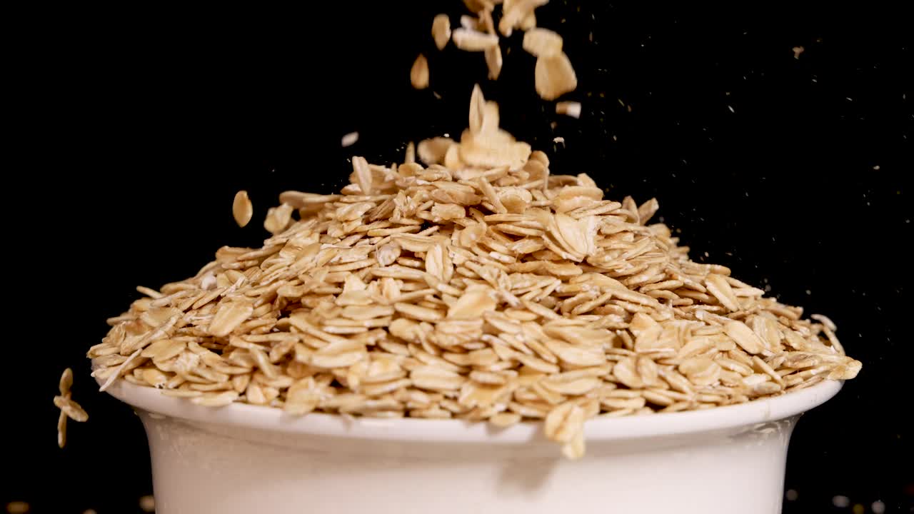 Oat grains cascade into a white bowl against a black background, highlighting texture and motion in a 26-second sequence
