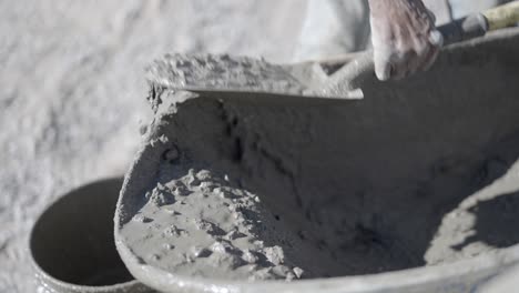 Construction-worker-shovels-dripping-wet-concrete-from-wheelbarrow-into-bucket