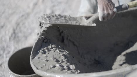 trabajador de la construcción palas chorreando hormigón húmedo de la carretilla en el balde