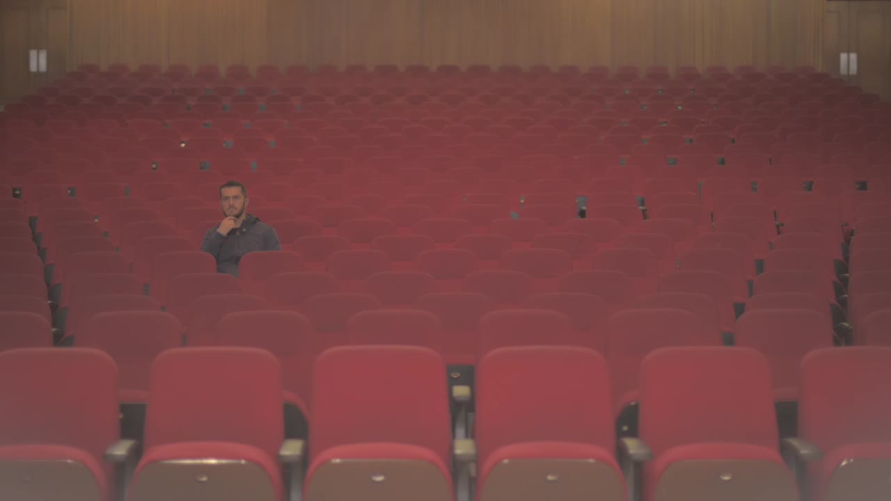 A tall white guy enters in an empty theatre. He takes a sit and he is the only one watching the show. He starts to see and enjoy the show that he sees on stage