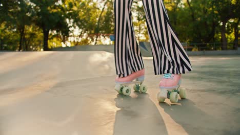 disparo en primer plano de una persona con pantalones a rayas y patines rosados montando en un piso de hormigón en un parque de patinaje en verano