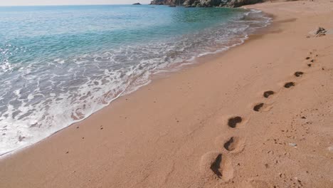 Menschlicher-Fußabdruck-An-Einem-Sandstrand-Neben-Meereswellen-In-Zeitlupe