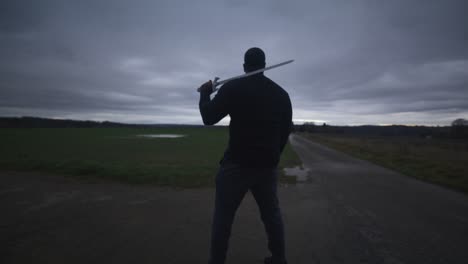 Modern-Black-Swordsman-Warrior-Awaiting-Battle-Opponent-in-Open-Field-Under-Grey-Sky,-Europe,-4K-|-Muscular,-Intimidating,-Shadow,-Figure,-Blurry,-Dark-Clothes,-Powerful,-Guarding,-Searching