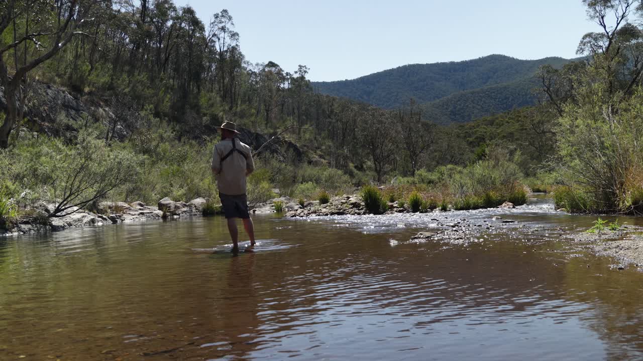 un bosquimano pescando trucha en un río victoriano de alto país con montañas en el fondo