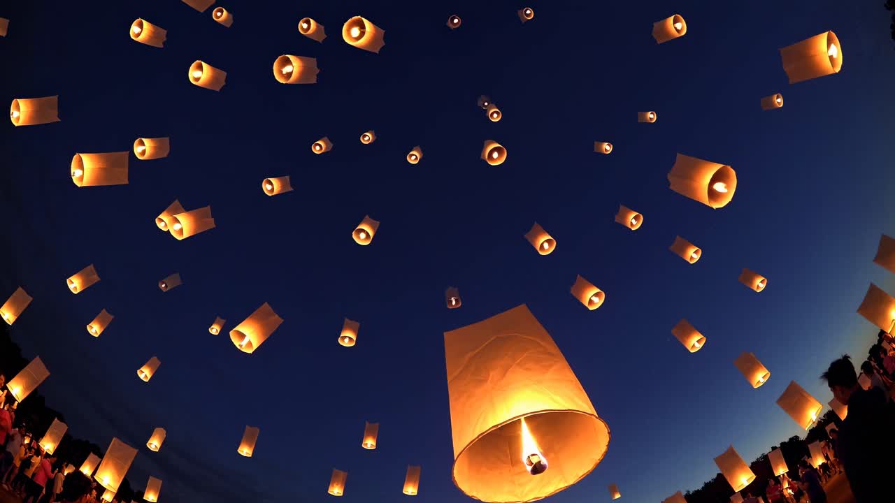 A mesmerizing video of glowing lanterns ascending into a deep blue sky, captured from a low-angle