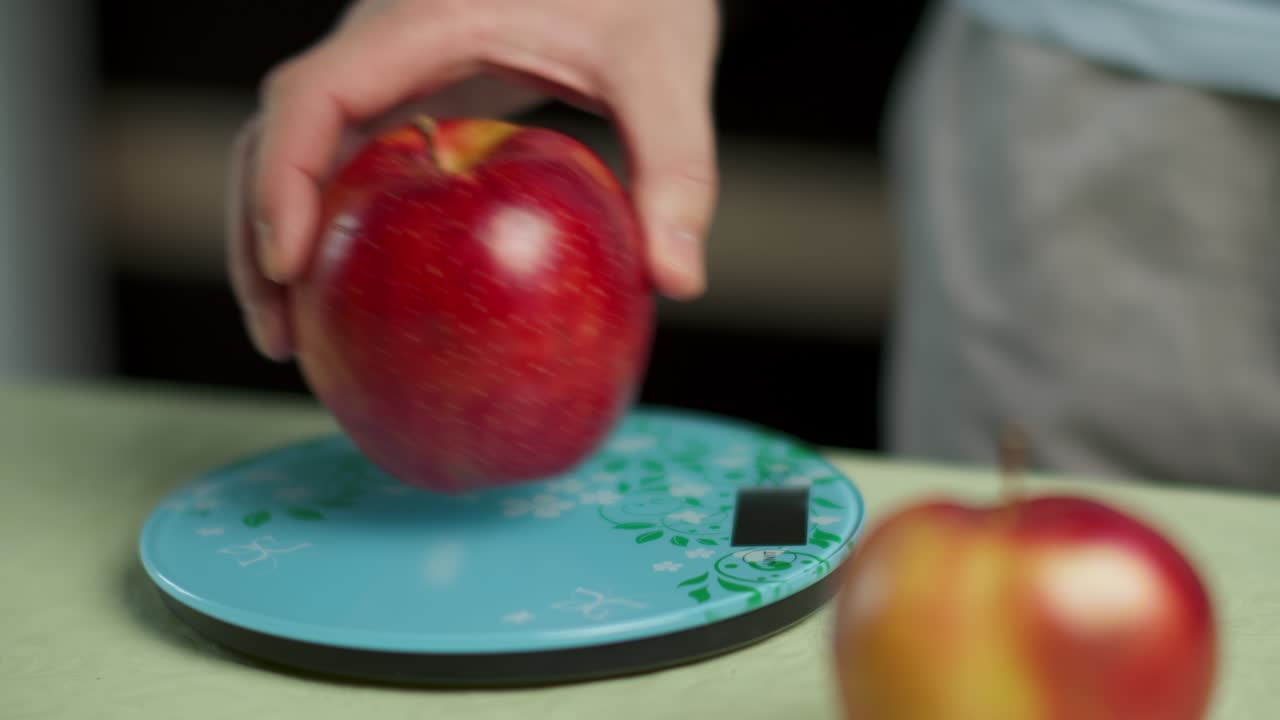 la mano de un hombre pesa varias manzanas rojas en una escala de cocina, de cerca