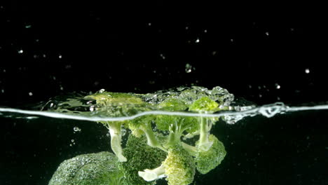 broccoli falling in water on black background