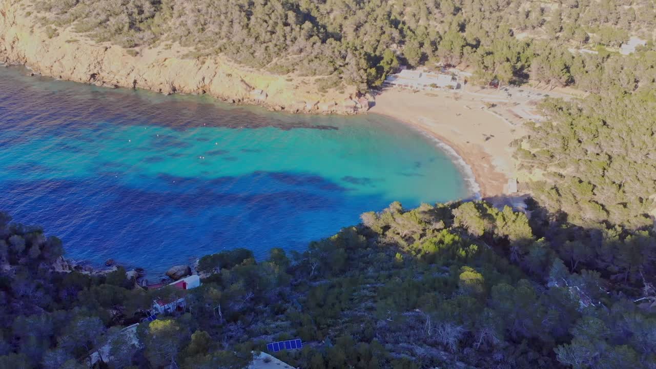 Filmagem de drone avançando em direção a uma pequena praia em uma pequena baía em Ibiza