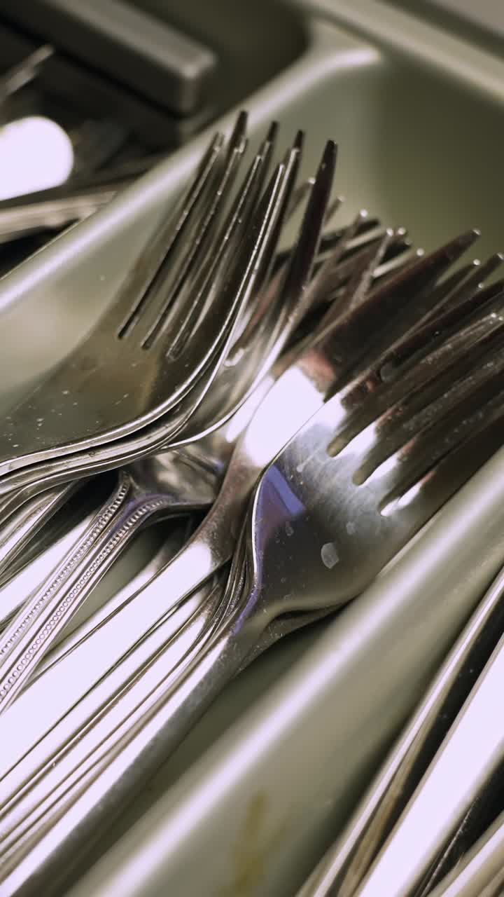 Close-up of stainless steel forks stacked in a dishwasher cutlery basket, kitchen cleanup and dishwashing routine, home hygiene and daily chores
