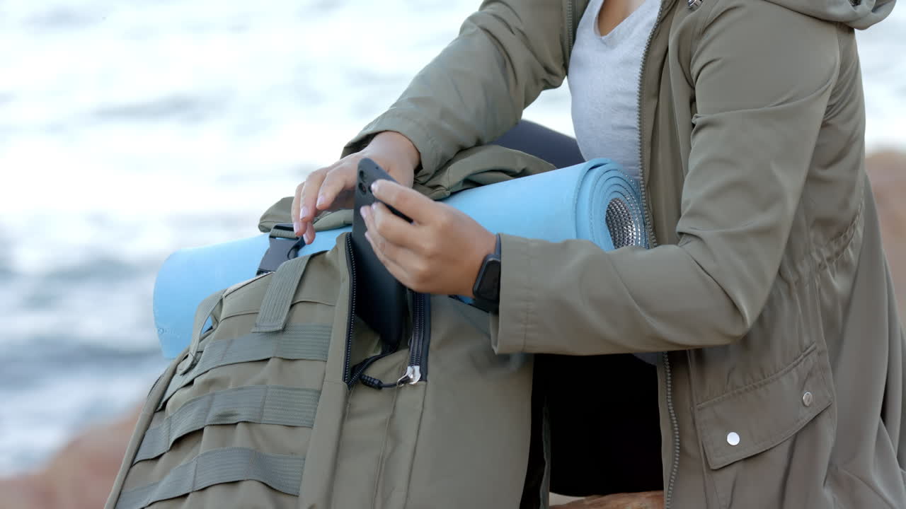 Using smartphone, woman sitting with backpack and yoga mat during mountain hike