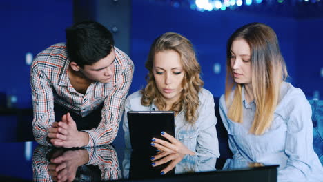 Junge-Leute-Entspannen-Sich-In-Einem-Café,-Während-Die-Drei-Auf-Den-Tablet-Bildschirm-Schauen