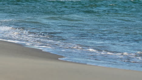 Ocean-waves-gently-crashing-onto-shore-with-white-foam,-peaceful-and-serene