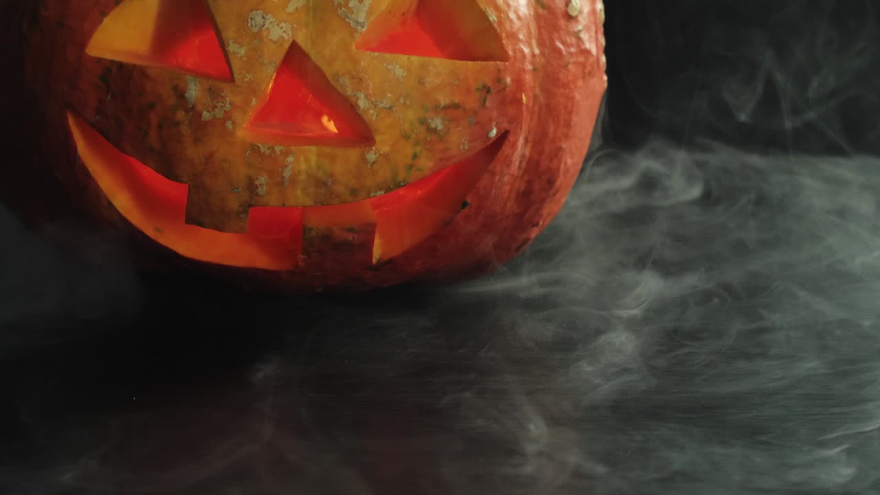 cargada halloween calabaza jack-o-lanterna con velas en ella en la mesa oscura con humo blanco en la parte superior. movimiento lento. disparo de primer plano. 4k