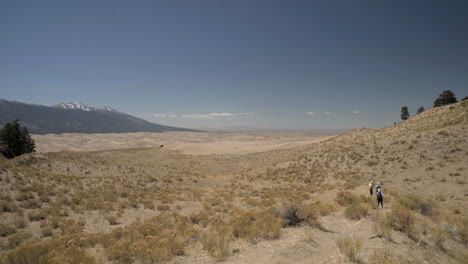 hikers walk down path towards great sand dunes national park in distance